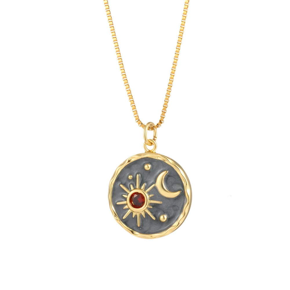 A gold and black celestial-inspired pendant necklace featuring a textured circular design with a radiant sun and crescent moon motif. The sun is adorned with a vibrant red gemstone at its center, creating an elegant and timeless accessory.