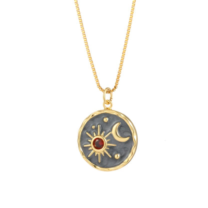 A gold and black celestial-inspired pendant necklace featuring a textured circular design with a radiant sun and crescent moon motif. The sun is adorned with a vibrant red gemstone at its center, creating an elegant and timeless accessory.